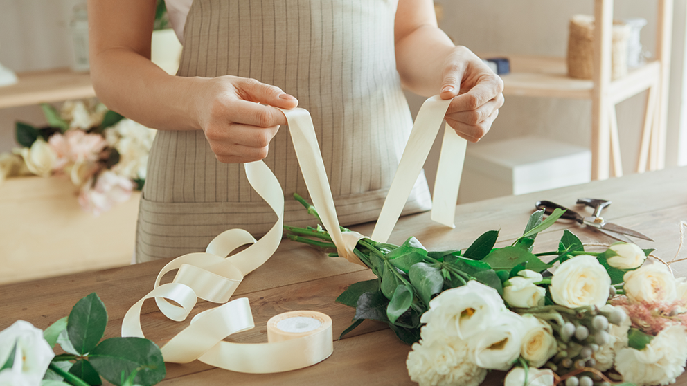 Woman tiering a bow around wedding flowers.