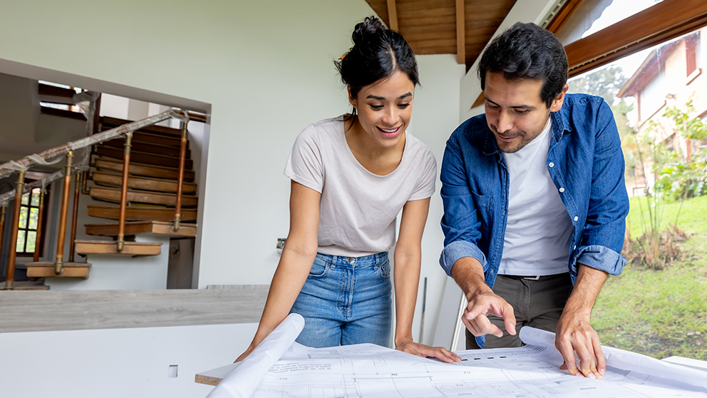 two young adults looking at home building blueprints
