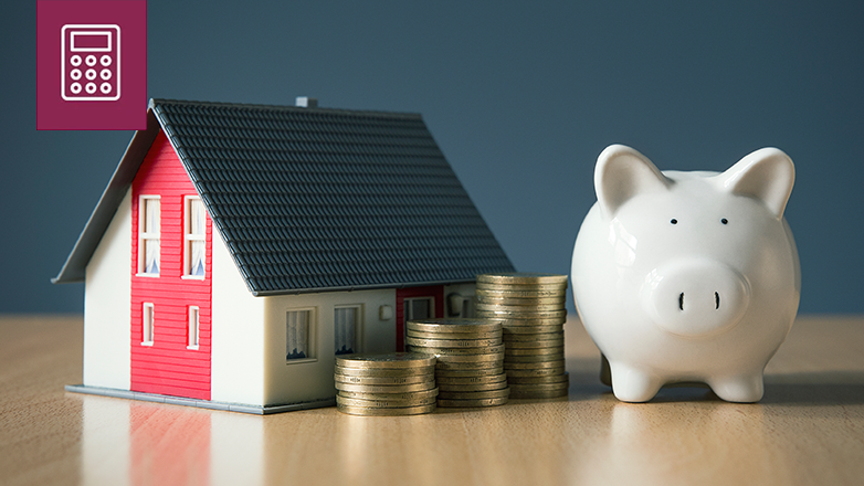 A piggy bank sits next to a small model house. Stacks of coins are in front of the house.